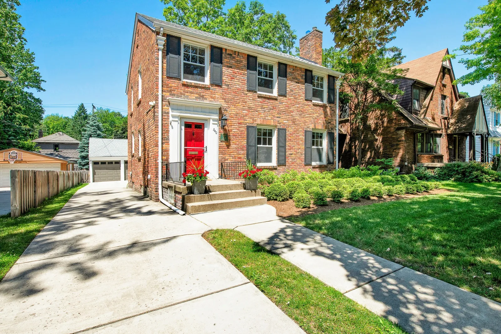 Brick colonial home with a red front door on a tree-lined street, residential real estate photography in Detroit