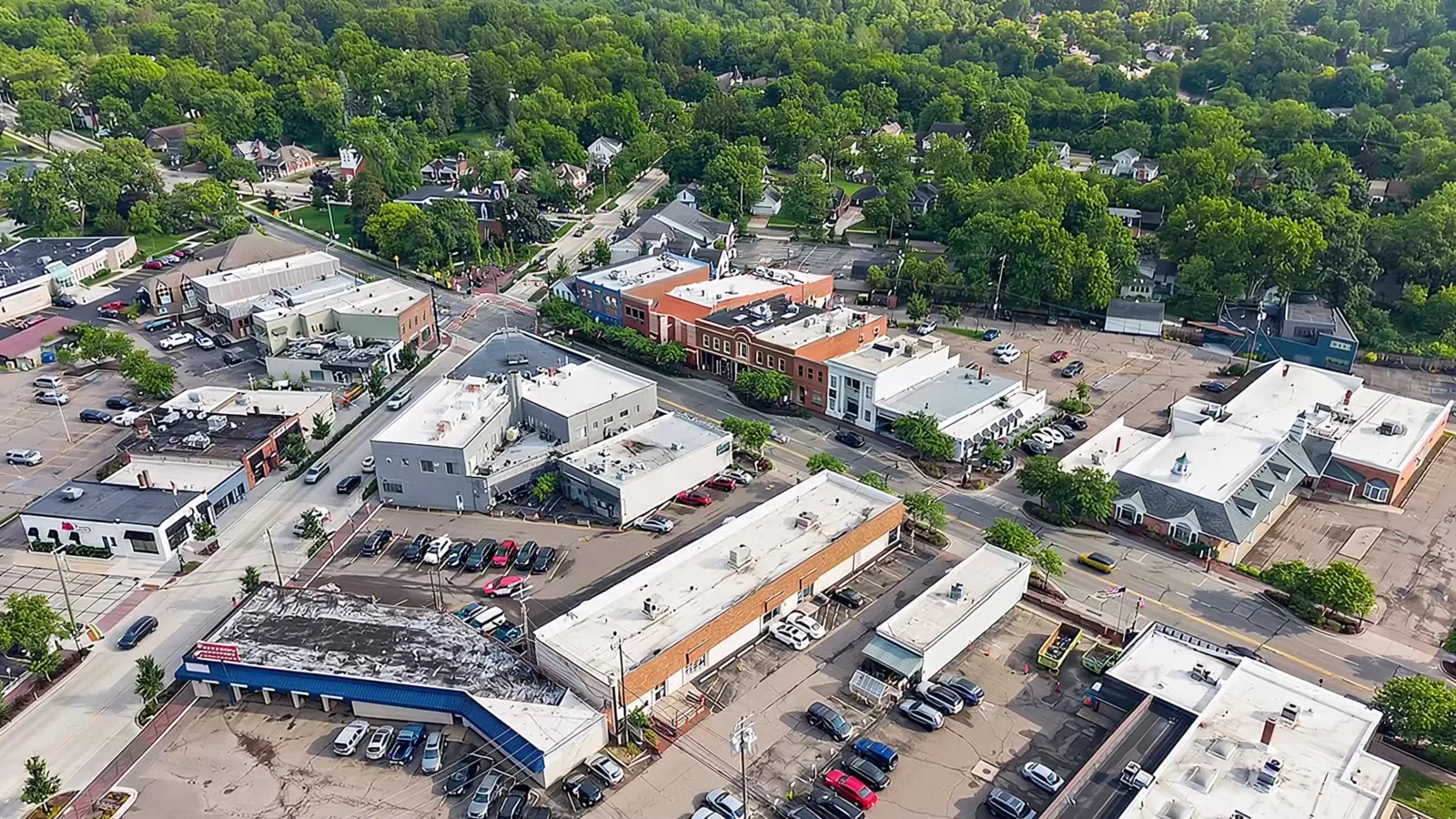 Aerial drone view of a small downtown commercial strip surrounded by trees in Farmington Hills, Michigan